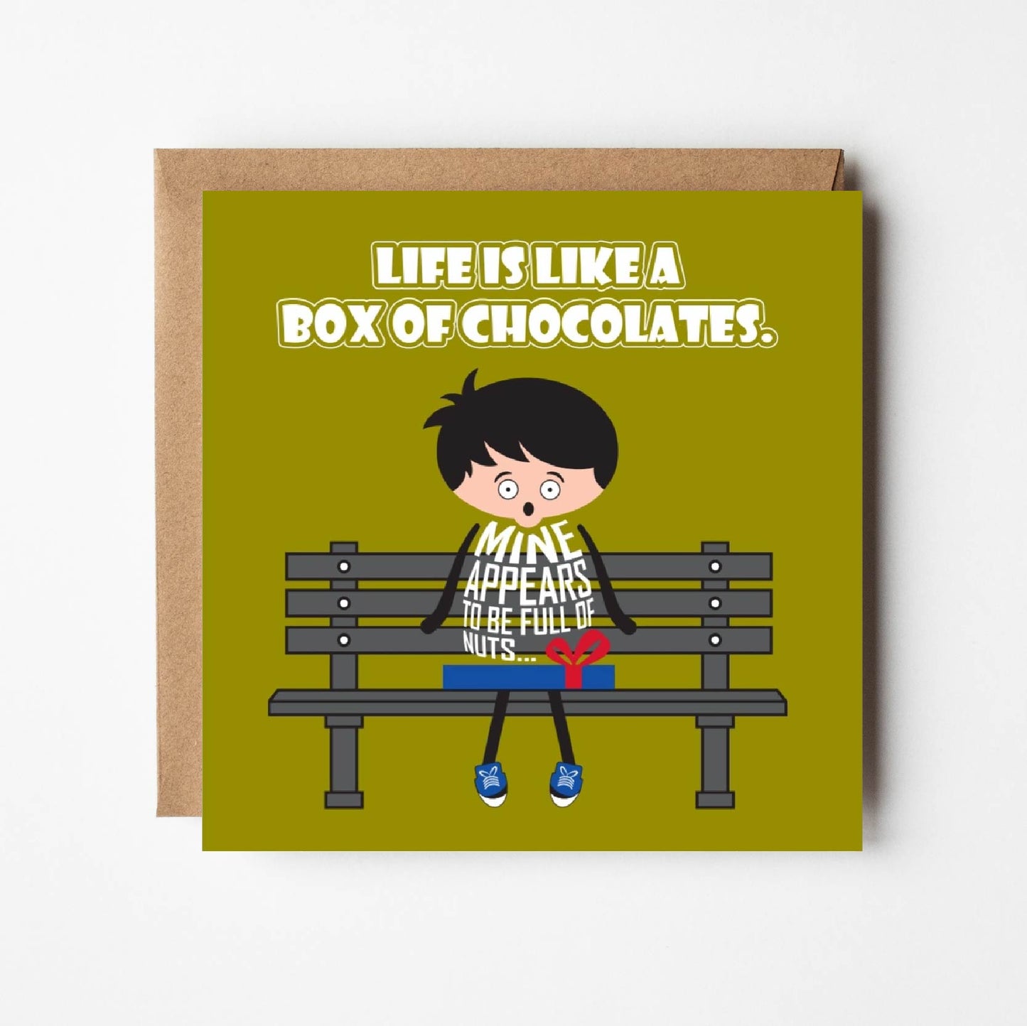 Card titled “Life is like a box of chocolates” in white text on a green background. A cartoon man sits on a park bench with a box of chocolates on his knee just like the the iconic scene from Forrest Gump. In a reference to both life and his box of chocolates, the man observes that “Mine appears to be full of nuts.”