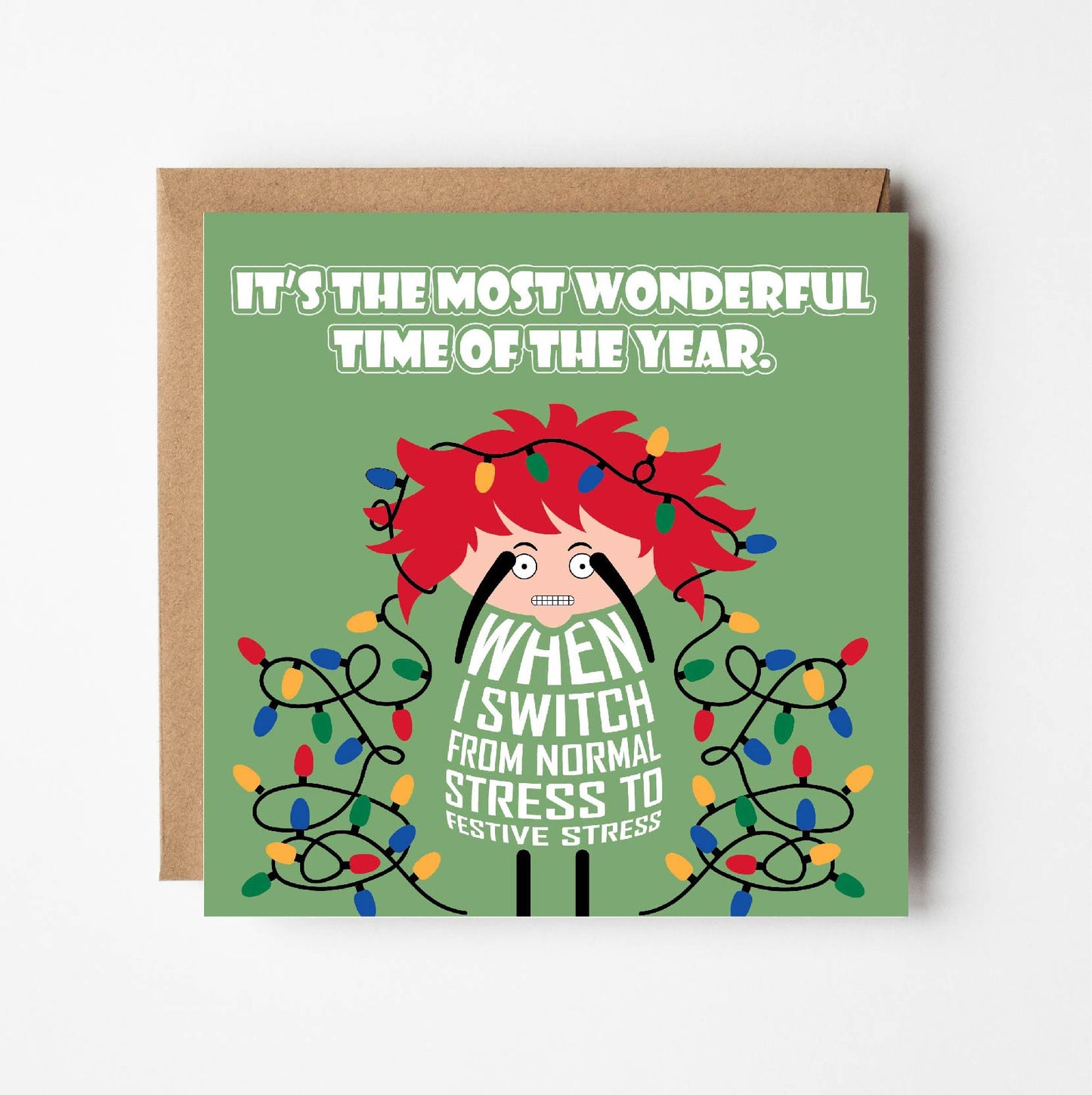 Card titled It’s the Most Wonderful Time of Year in white text on green background. A lady with Christmas lights tangled in her wild red hair quips that it is When I switch from normal stress to festive stress. Card is 150mm square with eco-Kraft envelope.