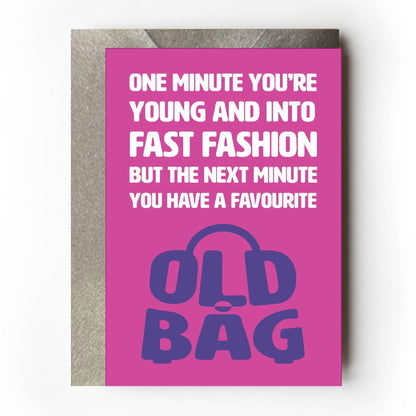 Text on card is white and purple against a pink background and states "One minute you're young and into fast fashion but the next minute you have a favourite old bag"   The 'old bag' text is in the shape of an old bag.  Card measures 105 x 150mm and is supplied with a very striking pewter-effect eco-Kraft envelope.