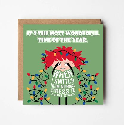 Card titled It’s the Most Wonderful Time of Year in white text on green background.  A lady with Christmas lights tangled in her wild red hair quips that it is When I switch from normal stress to festive stress. Card is 150mm square with eco-Kraft envelope.    