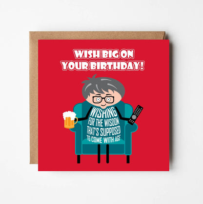 Card titled “Wish big on your birthday!” in white text on red background.  A cartoon man sits in armchair with a beer. His shirt says “Wishing for the wisdom that's supposed to come with age”  Card is 150mm square with a eco-Kraft envelope. 