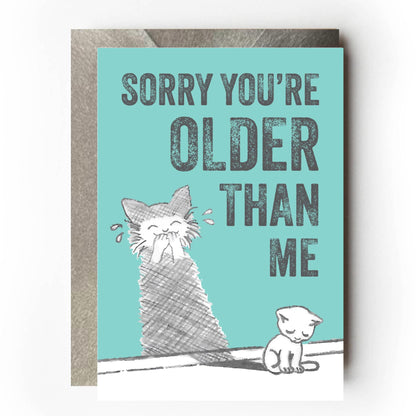 Sad-looking cat sitting beside a wall where its shadow appears to be laughing mischievously. Text reads: “Sorry you’re older than me” Funny sarcastic birthday card design for cat lovers.