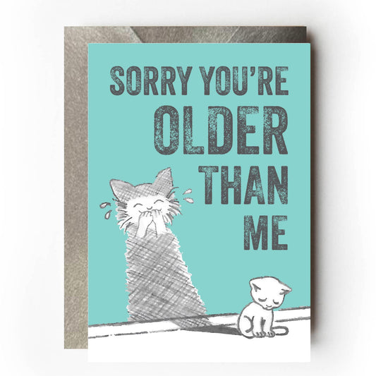 Sad-looking cat sitting beside a wall where its shadow appears to be laughing mischievously. Text reads: “Sorry you’re older than me” Funny sarcastic birthday card design for cat lovers.